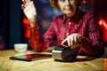 Mature female doing POS terminal and smartphone payment transaction in evening at coffee shop table. Senior customer using Royalty Free Stock Photo