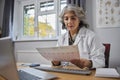 Mature Female GP Wearing White Coat At Desk In Doctors Office Look At ECG Readout Royalty Free Stock Photo