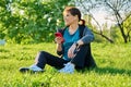 Mature female in headphones with smartphone listening music, sitting on grass Royalty Free Stock Photo