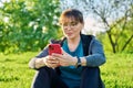 Mature female in headphones with smartphone watching video, sitting on grass Royalty Free Stock Photo