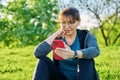 Mature female in headphones with smartphone watching video, sitting on grass Royalty Free Stock Photo