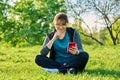 Mature female in headphones with smartphone watching video, sitting on grass Royalty Free Stock Photo