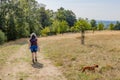 Mature female hiker in casual clothing walking with her dachshund on a trail surrounded by brown green grass