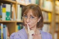 Mature female librarian giving a sign to be quiet standing in library