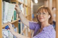 Mature female librarian taking a book off a shelf