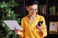 Middle aged businesswoman using smartphone and reading data on paper