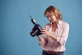 Mature Female Photographer With Camera Against Blue Background On Shoot In Studio