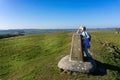 Mature female rambler admiring beautiful hilltop view from a triangulation point or trig point on White Sheet Hill in Wiltshire Royalty Free Stock Photo