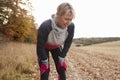 Mature Female Runner Pausing For Breath During Exercise In Woods