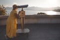 Mature female traveler looks through tourist binocular at mountains and sea. Concept of traveling for retired persons.