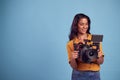 Mature Female Videographer With Camera Filming Video Against Blue Background On Shoot In Studio