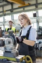 Mature female worker working on machinery with colleague in background at factory Royalty Free Stock Photo