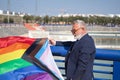 Mature gay man, executive, gray haired, with beard, sunglasses, jacket and tie, proudly showing new lgbtiq+ pride flag. Concept