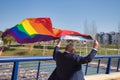 Mature gay man, executive, gray haired, with beard, sunglasses and jacket, walking with new lgbtiq+ pride flag in the wind above
