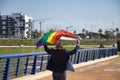 Mature gay man, executive, gray haired, with beard, sunglasses and jacket, walking with new lgbtiq+ pride flag in the wind above