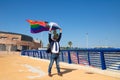 Mature gay man, executive, grey-haired, bearded, sunglasses, jacket and tie, waving the new lgbtiq+ pride flag in the wind under a