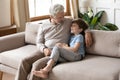 Mature grandfather talking with adorable grandson, sitting on couch