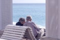 A mature, gray-haired beautiful couple: a man and a woman are sitting on a white bench on the Promenade des Anglais and looking a