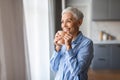 Mature gray lady with haircut sips tea holding cup indoor