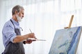 mature grey haired artist man painting using painter palette