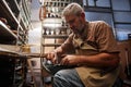 Mature grey-haired male master of shoemaking putting shoelace into boot