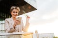 Mature grey woman smiling and using mobile phone on balcony