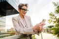 Mature grey woman smiling and using mobile phone on balcony