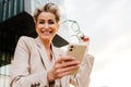 Mature grey woman smiling and using mobile phone on balcony