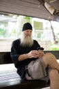 Mature handsome bearded hipster man using phone while sitting on wooden bench Royalty Free Stock Photo