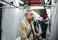 Mature businessman with smartphone travelling by subway in city. Royalty Free Stock Photo