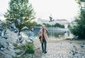 Mature businessman walking by river Vltava in Prague city, dispersing pigeons.