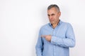 Mature handsome confused man with grey hair wearing blue shirt standing on isolated white background points with his Royalty Free Stock Photo