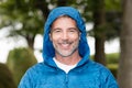 Mature handsome man wearing windbreaker with hood on smiling at the camera. Outside.