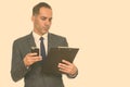 Mature handsome Persian businessman reading clipboard while holding mobile phone Royalty Free Stock Photo