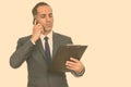 Mature handsome Persian businessman reading clipboard while talking on mobile phone Royalty Free Stock Photo