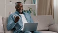 Mature happy african american man sitting on sofa at home relaxing smiling chatting on laptop via webcam talking on Royalty Free Stock Photo