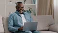 Mature happy african american man sitting on sofa at home relaxing smiling chatting on laptop via webcam talking on Royalty Free Stock Photo