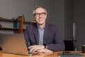 Mature happy businessman in eye glasses and suit is smiling sitting by the  laptop in office Royalty Free Stock Photo