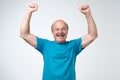 Mature hispanic man in blue t-shirt celebrating victory of his team over gray background. Royalty Free Stock Photo