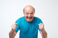 Mature hispanic man in blue t-shirt celebrating victory of his team over gray background. Royalty Free Stock Photo