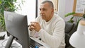 Mature hispanic man in thoughtful pose at office workplace staring at computer screen Royalty Free Stock Photo