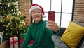 Mature hispanic woman with grey hair taking a selfie picture sitting on the sofa at home