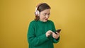 Mature hispanic woman with grey hair using smartphone wearing headphones over isolated yellow background Royalty Free Stock Photo