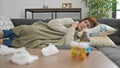 Mature hispanic woman lying on the sofa sick with tissues and pills on the table at home