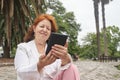 Mature hispanic woman reading an ebook on an electronic reader sitting in a park Royalty Free Stock Photo