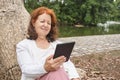 Mature hispanic woman reading an ebook on an electronic reader sitting in a park Royalty Free Stock Photo