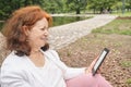 Mature hispanic woman reading an ebook on an electronic reader sitting in a park Royalty Free Stock Photo