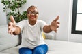 Mature hispanic woman sitting on the sofa at home looking at the camera smiling with open arms for hug Royalty Free Stock Photo