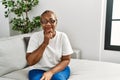 Mature hispanic woman sitting on the sofa at home looking confident at the camera with smile with crossed arms and hand raised on Royalty Free Stock Photo