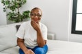 Mature hispanic woman sitting on the sofa at home looking confident at the camera smiling with crossed arms and hand raised on Royalty Free Stock Photo